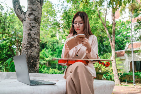 A young Asian woman gracefully practices the violin in a peaceful outdoor setting surrounded by lush greenery. Capturing a moment of musical concentration and tranquillity in nature.の写真素材