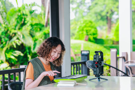 Asian woman with curly, two-tone hair engages in online music session using a small keyboard and...