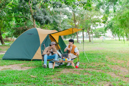 Two Asian male friends relax by the lake, enjoying music and singing together in serene outdoor setting. The scene captures joyful and peaceful moment of bonding and creativity during camping tripの写真素材