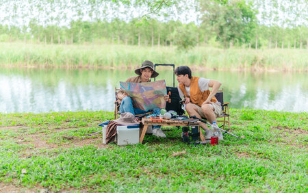 Two Asian male friends enjoy a calm camping experience beside a lake, surrounded by nature and gear. The scene captures a relaxed moment of outdoor exploration and preparation in a scenic setting.の写真素材