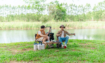Two Asian male friends enjoy a calm camping experience beside a lake, surrounded by nature and gear....