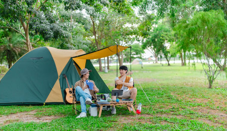 Two Asian male friends enjoy relaxing moment together at campsite surrounded by nature. With a tent set up and gear around them, the atmosphere reflects leisure, companionship, and outdoor freedomの写真素材