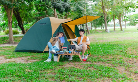 Two Asian male friends enjoy relaxing moment together at campsite surrounded by nature. With a tent set up and gear around them, the atmosphere reflects leisure, companionship, and outdoor freedomの写真素材
