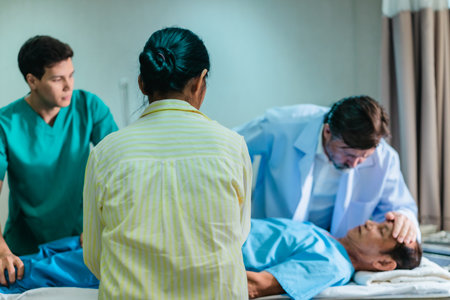 A concerned woman speaks with medical professionals beside a patient lying in a hospital bed. The...