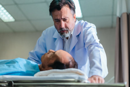 Senior physician carefully examines patient's vital signs while the patient lies in a hospital bed,...