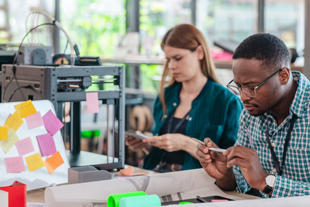 A diverse team of startup professionals collaborates on a 3D printing project in a modern workspace....