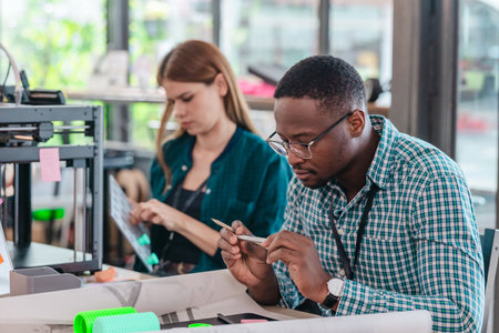 A diverse team of startup professionals collaborates on a 3D printing project in a modern workspace. Highlighting innovation, teamwork, and the prototyping process in a creative tech environment.の写真素材