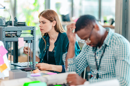 A diverse team of startup professionals collaborates on a 3D printing project in a modern workspace....