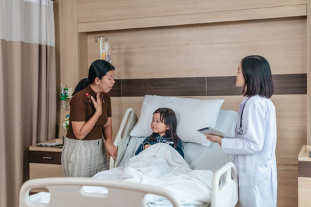 Caring Asian female doctor checks on young girl in hospital bed during consultation, while child's mother provide support and comfort. warmth, trust, and professional medical care in clinical settingの写真素材