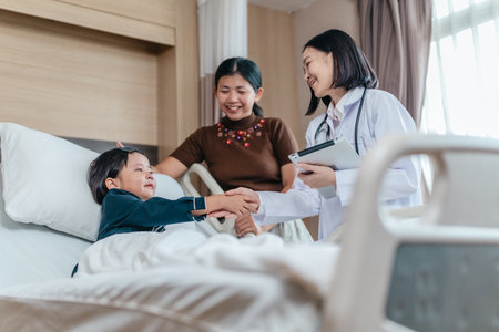 Caring Asian female doctor checks on young girl in hospital bed during consultation, while child's mother provide support and comfort. warmth, trust, and professional medical care in clinical settingの写真素材