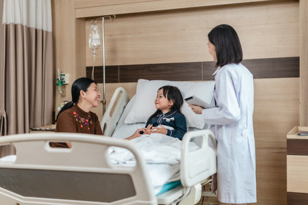 Caring Asian female doctor checks on young girl in hospital bed during consultation, while child's mother provide support and comfort. warmth, trust, and professional medical care in clinical settingの写真素材