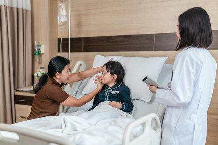 Caring Asian female doctor checks on young girl in hospital bed during consultation, while child's mother provide support and comfort. warmth, trust, and professional medical care in clinical settingの写真素材