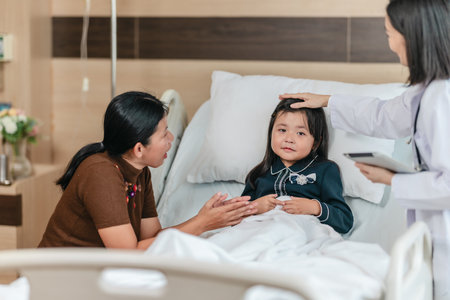Caring Asian female doctor checks on young girl in hospital bed during consultation, while child's mother provide support and comfort. warmth, trust, and professional medical care in clinical settingの写真素材