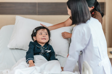 Caring Asian female doctor checks on young girl in hospital bed during consultation, while child's mother provide support and comfort. warmth, trust, and professional medical care in clinical settingの写真素材