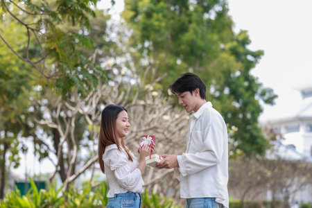 An Asian couple shares a joyful moment while exchanging gift boxes in a scenic outdoor setting. The scene captures feelings of love, celebration, and connection during a special occasion.の写真素材