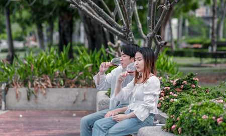 Asian couple shares tender moment as man gives necklace to his partner during Valentines Day celebration. Joyful expressions and natural surroundings highlight romance and significance of occasion.の写真素材