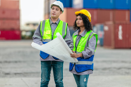 Industrial container workers discuss sustainable logistics operations. Analyzing blueprint,...