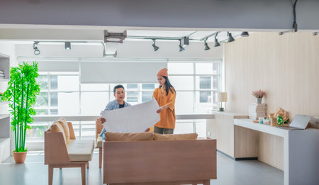 Two professionals review a large planning sheet together in a bright, modern workspace. The scene reflects teamwork, strategic thinking, and collaborative project development in a startup environmentの写真素材