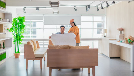 Two professionals review a large planning sheet together in a bright, modern workspace. The scene reflects teamwork, strategic thinking, and collaborative project development in a startup environmentの写真素材