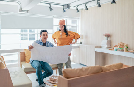 Two professionals review a large planning sheet together in a bright, modern workspace. The scene reflects teamwork, strategic thinking, and collaborative project development in a startup environmentの写真素材