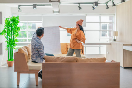 Two professionals review a large planning sheet together in a bright, modern workspace. The scene reflects teamwork, strategic thinking, and collaborative project development in a startup environmentの写真素材