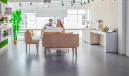 Two professionals review a large planning sheet together in a bright, modern workspace. The scene...