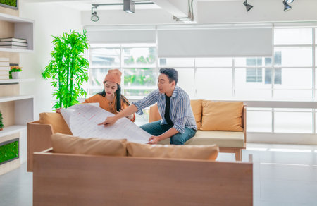 Two professionals review a large planning sheet together in a bright, modern workspace. The scene reflects teamwork, strategic thinking, and collaborative project development in a startup environmentの写真素材