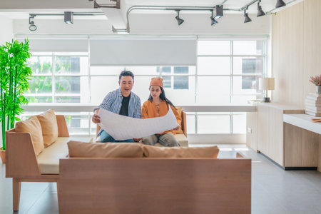 Two professionals review a large planning sheet together in a bright, modern workspace. The scene reflects teamwork, strategic thinking, and collaborative project development in a startup environmentの写真素材