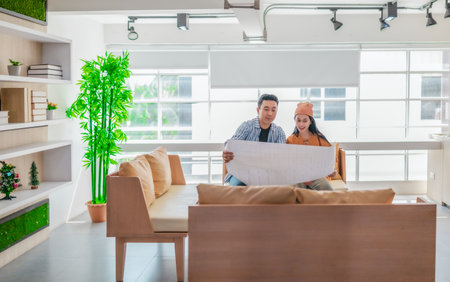 Two professionals review a large planning sheet together in a bright, modern workspace. The scene reflects teamwork, strategic thinking, and collaborative project development in a startup environmentの写真素材