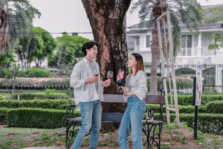 Asian couple enjoys heartfelt moment on park bench as man presents bouquet of red flowers and gift...