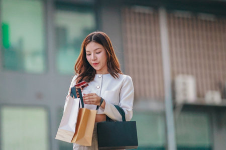Asian woman smiles while holding eco-friendly, reusable shopping bags in urban setting, promoting sustainable consumer behavior. Highlighting concepts like green shopping, recycling, circular economyの写真素材