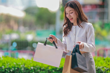 Asian woman smiles while holding eco-friendly, reusable shopping bags in urban setting, promoting...