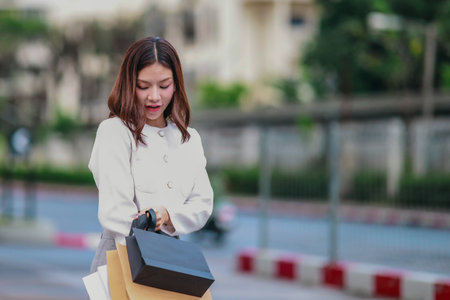 Asian woman smiles while holding eco-friendly, reusable shopping bags in urban setting, promoting sustainable consumer behavior. Highlighting concepts like green shopping, recycling, circular economyの写真素材