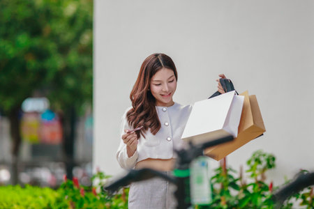 Asian woman smiles while holding eco-friendly, reusable shopping bags in urban setting, promoting sustainable consumer behavior. Highlighting concepts like green shopping, recycling, circular economyの写真素材