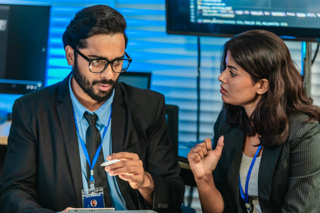 Two professionals analyze and discuss programming code displayed on screen in modern tech workspace....