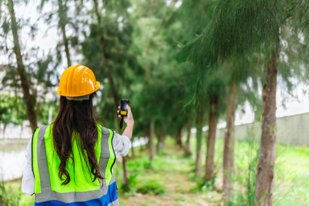 Female environmental fieldworker uses GPS land meter to survey tree positions, spacing, height in forest area. Environmental monitoring, sustainable land management, and integration of digital toolsの写真素材