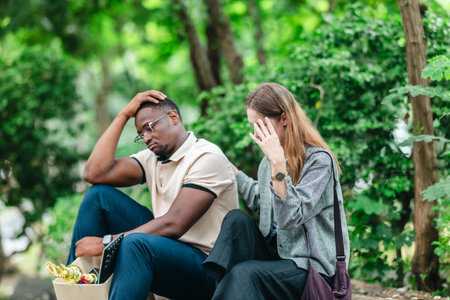 African male employee carries box of office belongings while female coworker encourages him outdoors. Reflecting job loss during an economic downturn and power of workplace support and resilienceの写真素材