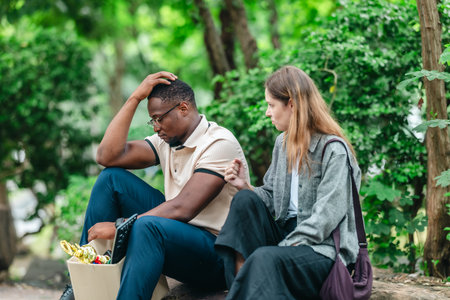 African male employee carries box of office belongings while female coworker encourages him outdoors. Reflecting job loss during an economic downturn and power of workplace support and resilienceの写真素材