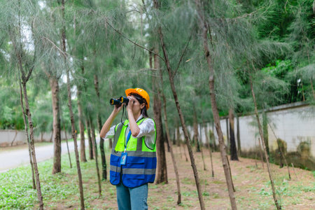 Female environmental surveyor observes forest conditions using binoculars, takes notes, communicates data. Environmental monitoring, biodiversity tracking, role of women in filed forest assessment.の写真素材
