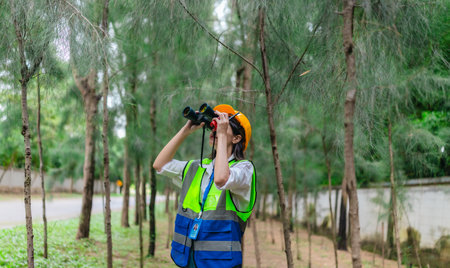 Female environmental surveyor observes forest conditions using binoculars, takes notes, communicates data. Environmental monitoring, biodiversity tracking, role of women in field forest assessment.の写真素材