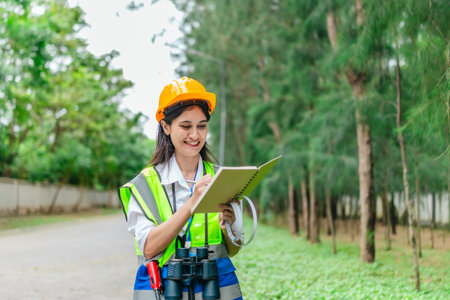 Female environmental surveyor observes forest conditions using binoculars, takes notes, communicates data. Environmental monitoring, biodiversity tracking, role of women in filed forest assessment.の写真素材