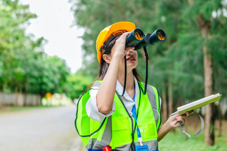 Female environmental surveyor observes forest conditions using binoculars, takes notes, communicates data. Environmental monitoring, biodiversity tracking, role of women in field forest assessment.の写真素材