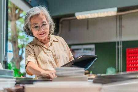 A senior Asian woman, the business owner, conducts quality control by visually inspecting ceramic...