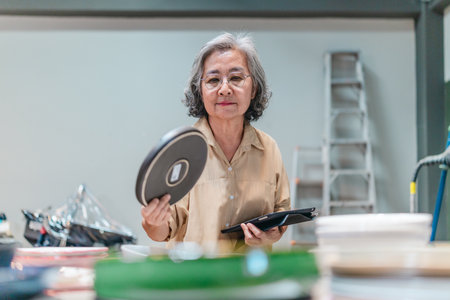 A senior Asian woman, the business owner, conducts quality control by visually inspecting ceramic...