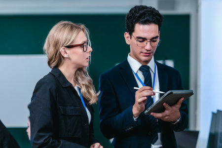 Two developers collaborate on code at workstation, reviewing printouts and screens in a modern tech office. Highlighting teamwork, mentoring, and debugging within a professional software environment.の写真素材