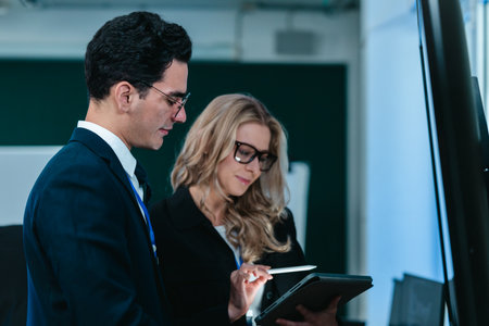 Two developers collaborate on code at workstation, reviewing printouts and screens in a modern tech office. Highlighting teamwork, mentoring, and debugging within a professional software environment.の写真素材