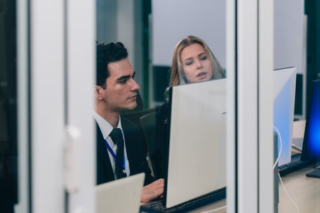 Two developers collaborate on code at workstation, reviewing printouts and screens in a modern tech office. Highlighting teamwork, mentoring, and debugging within a professional software environment.の写真素材