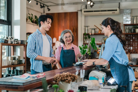 At a family run ceramic store, a mother and daughter provide friendly service to a male customer at the counter, highlighting warm retail hospitality and homeware shopping.の写真素材