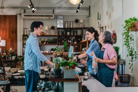 At a family run ceramic store, a mother and daughter provide friendly service to a male customer at the counter, highlighting warm retail hospitality and homeware shopping.の写真素材