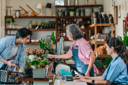 At a family run ceramic store, a mother and daughter provide friendly service to a male customer at the counter, highlighting warm retail hospitality and homeware shopping.の写真素材
